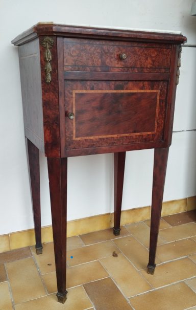 Table de chevet en bois, avec un tiroir, sur quatre pieds et des détails dorés.